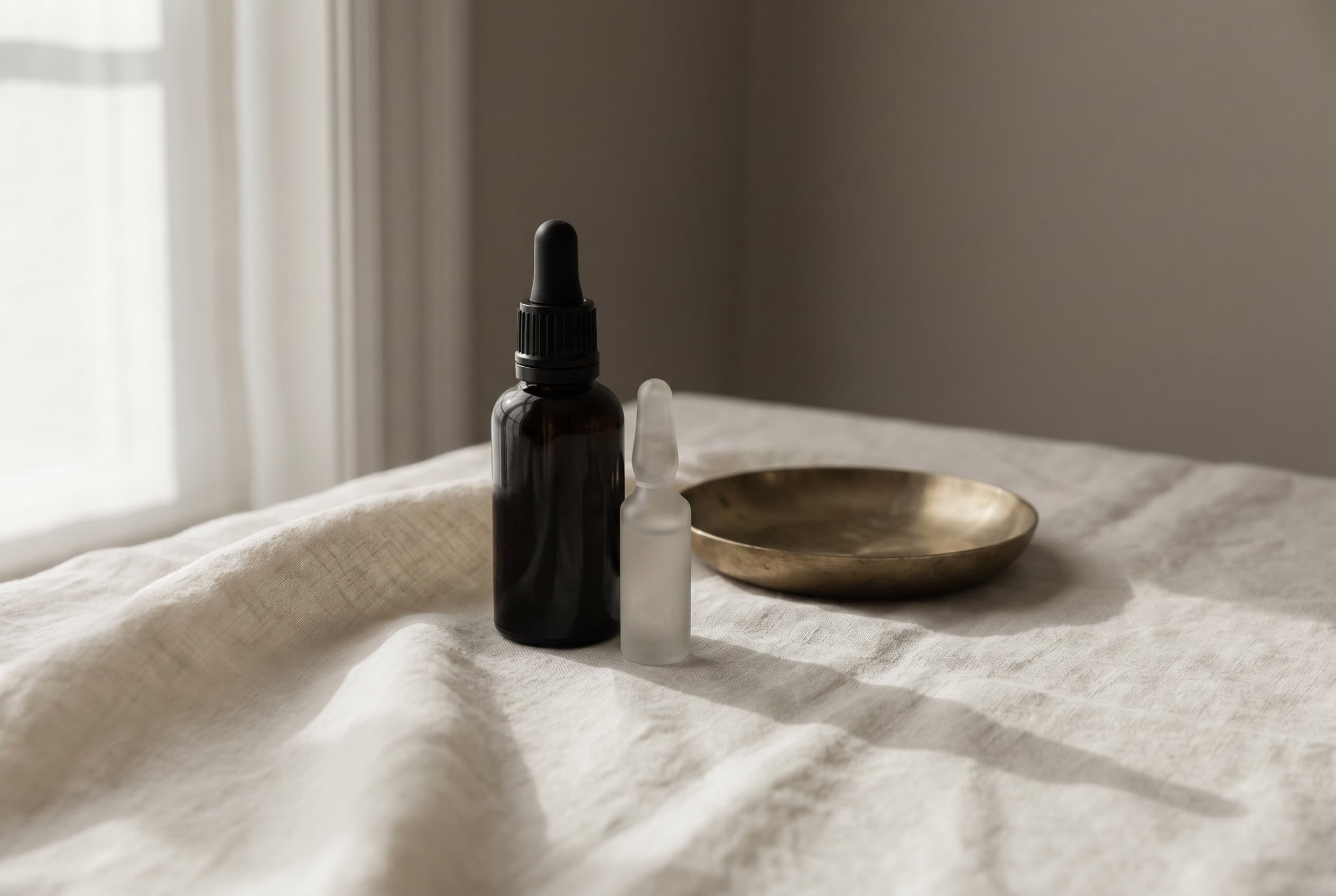 Two matched amber apothecary vials standing together on ivory linen in morning light.